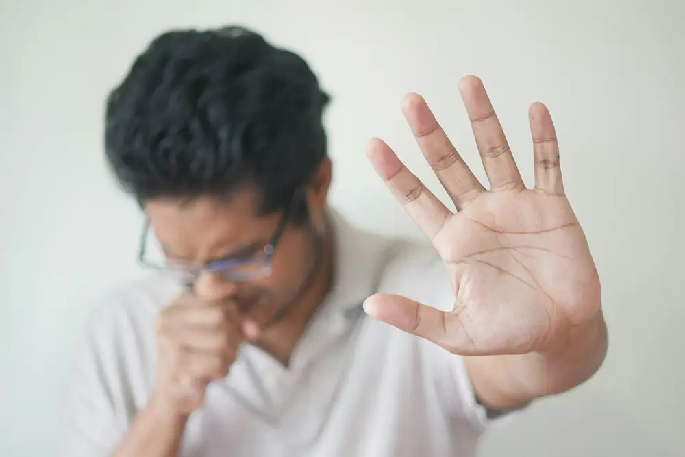 Homme toussant, faisant semblant d'être malade et mettant sa main ouverte devant soi pour bloquer