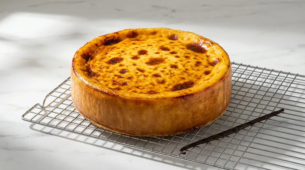 Flan parisien entier sur grille, surface caramélisée avec cloques dorées et gousse de vanille