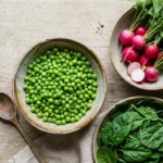 Saladier de petits pois frais, botte de radis roses et épinards verts sur fond de bois clair – légumes de printemps