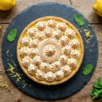 Tarte au citron meringuée entière sur une assiette en ardoise avec zestes de citron frais