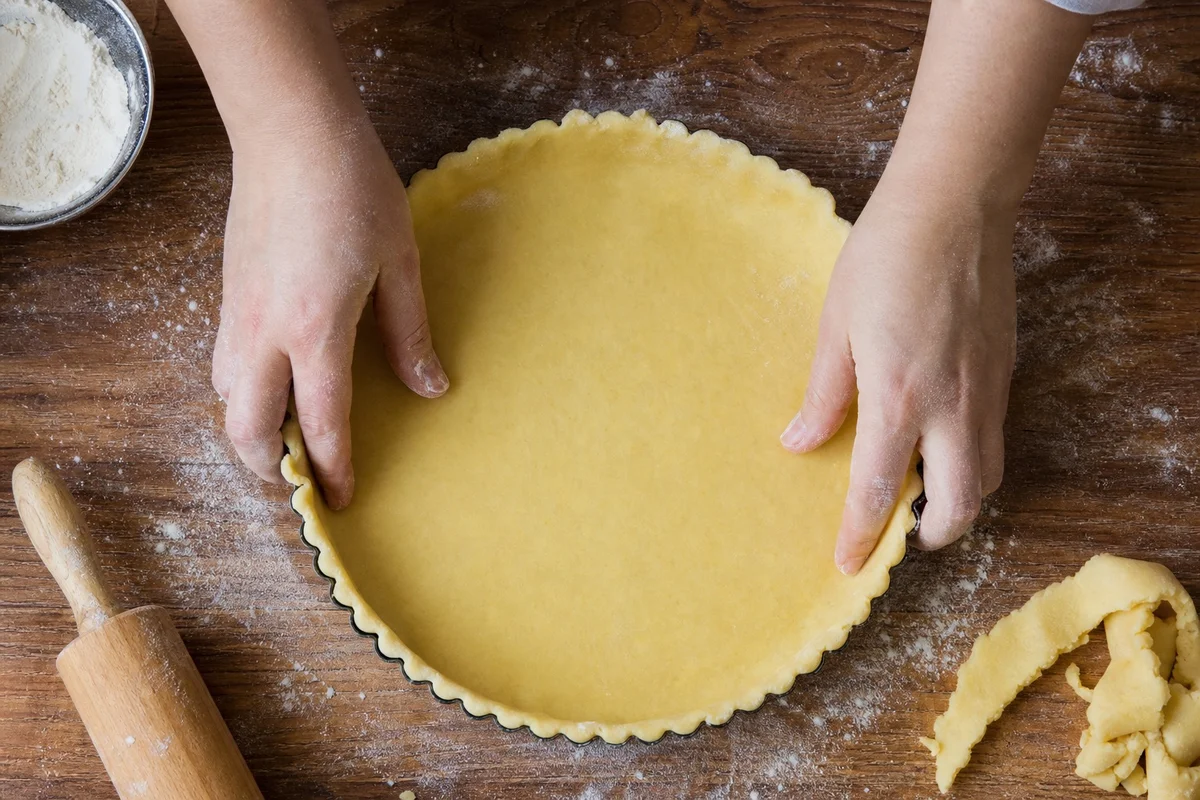 Pâte brisée étalée déposée délicatement dans un moule à tarte à bord cannelé sans être étirée
