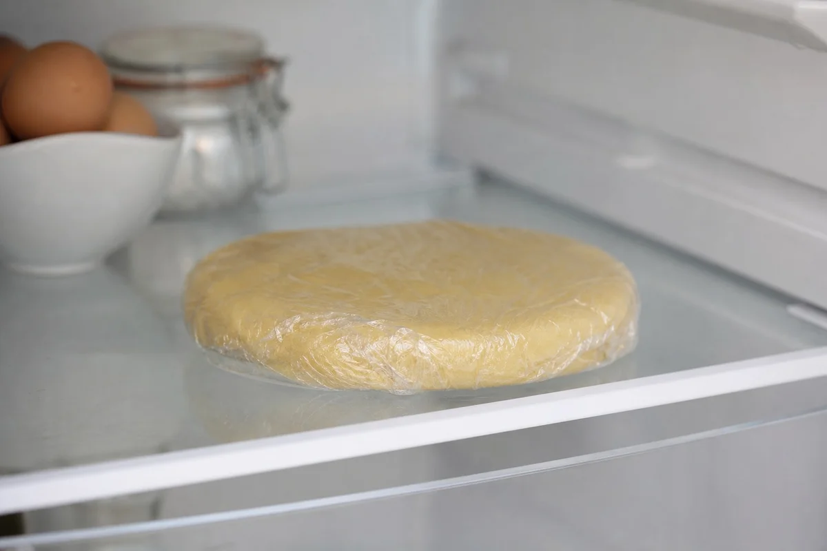 Disque de pâte brisée enveloppé de film alimentaire posé sur une clayette de réfrigérateur